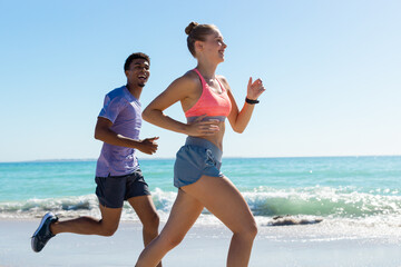 Obraz premium At beach, diverse couple jogging, both looking fit
