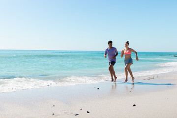 Obraz premium At beach, diverse couple running on sandy shore, enjoying sunny day