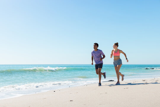 At beach, diverse couple running, enjoying time together