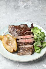 Pieces of delicious roasted beef meat, caramelized pear and greens on light textured table