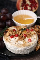 Plate with tasty baked camembert, honey, walnuts and pomegranate seeds on table, closeup