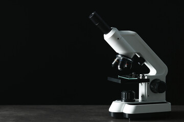 Modern microscope on grey table against black background, space for text