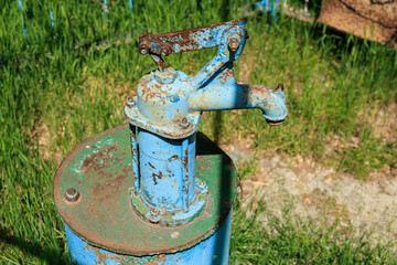 A rusty old water pump is sitting in a grassy field