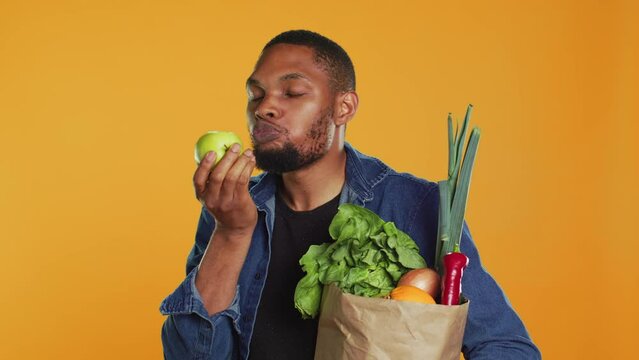 African american vegan guy taking a bite from a ripe natural green apple, eating freshly harvested organic fruits in studio. Person advertising local farming and ethically sourced goods. Camera A.