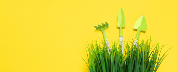 Yellow banner with green grass and gardening tools. Rake and shovels stick out of vegetation....