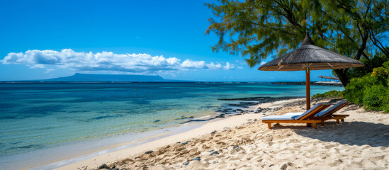 Tropical beach scene with lounge chairs under an umbrella, clear blue sky, and calm ocean waters.