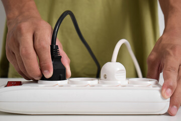 A man cuts off the electric current at a white electrical socket to reduce energy consumption