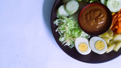 Gado-gado served on a plate, isolated white, Indonesian salad containing boiled vegetables and potatoes, boiled eggs, fried tofu tempeh, lontong and melinjo chips, served with peanut-cashew sauce. 