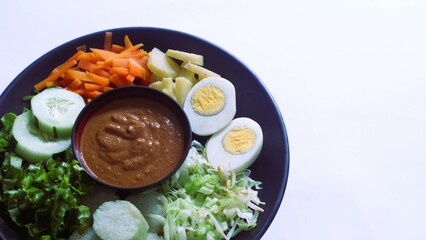 Gado-gado served on a plate, isolated white, Indonesian salad containing boiled vegetables and potatoes, boiled eggs, fried tofu tempeh, lontong and melinjo chips, served with peanut-cashew sauce. 