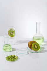 High angle shot photography with kiwi and lab glassware, an empty petri dish featured in the center, a little chopped kiwi and fresh kiwi placed on dish, green liquid in erlenmeyer and boiling flask