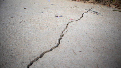 Crack in Concrete Surface The image shows a close-up view of a crack in a concrete surface. The crack is irregular and extends across the image. The concrete has a rough texture, with small pits and v