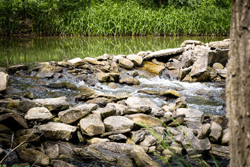 A stream flowing trough rocks next to a pond.