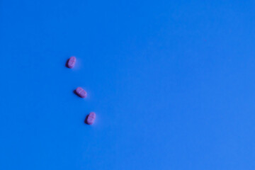 Three pink pills on a bright blue background.