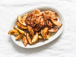 Delicious lunch, dinner - pork chop, baked new potatoes and caramelized onions in one plate on a light background, top view