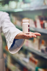 Pharmacist, hand and bottle for pills in store with by shelf for stock, show and inventory for...