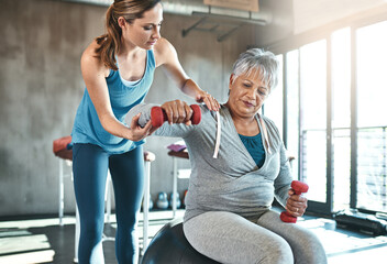 Senior woman, weights and helping with coach in gym for physio, arm exercise and rehabilitation on...