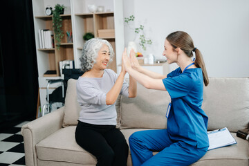 Young nurse helping elderly woman walk in the room, holding his hand, supporting. Treatment and rehabilitation after injury