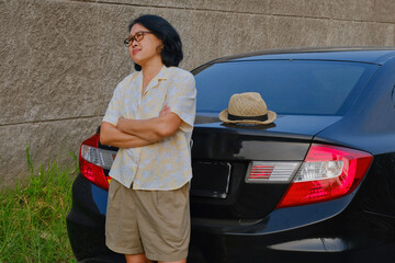 A woman is leaning against a car parked on the side of the road; bored, annoyed, upset expressions