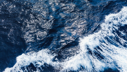 Waves crashing in deep blue sea with white surf foam. photo taken from top view. Waves forming due to ship movement