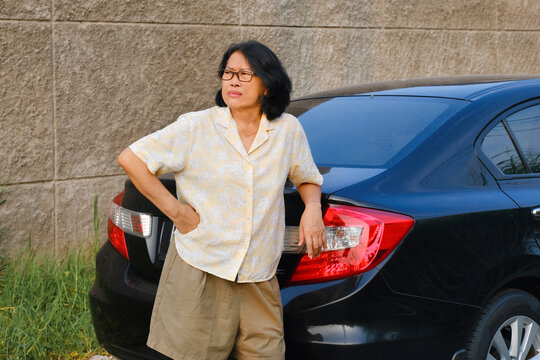 A woman is leaning against her car while looking at one side