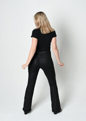Fototapeta premium Full length portrait of beautiful blonde woman wearing modern black shirt and leather pants. Confident standing pose walking away from camera, silhouetted on white studio background.