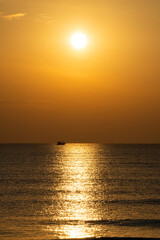 The sunset over the sea is a beautiful golden yellow glow, with fishing boats in the foreground.