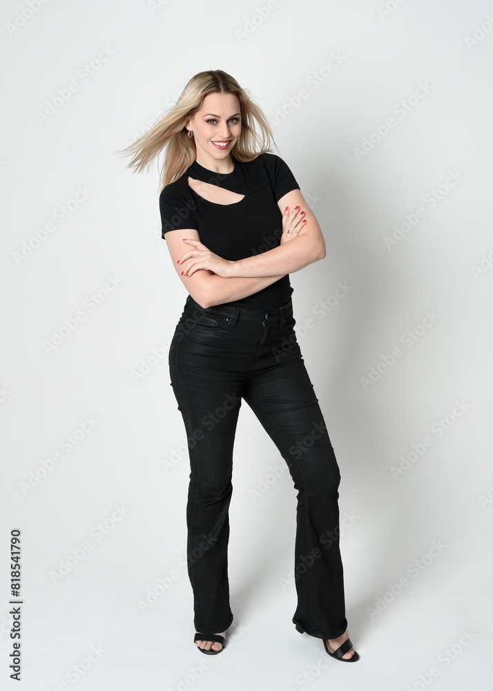 Sticker Full length portrait of beautiful blonde woman wearing modern black shirt and leather pants. Confident standing pose with gestural hands presenting, silhouetted on white studio background.