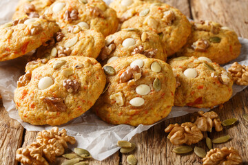 Autumn pumpkin cookies with white chocolate, nuts and seeds close-up on parchment on a wooden table. Horizontal