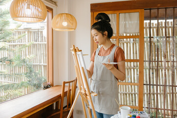 Asian young talented woman artist coloring on painting board in house. Attractive beautiful female...