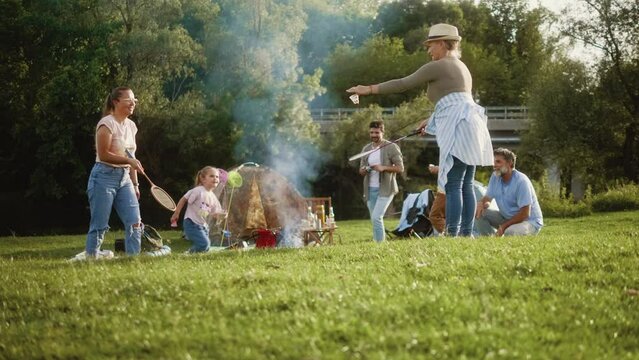 Medium shot of a multi-generational family camping in nature, playing bagminton, lighting a fire for barbecue and spending time together