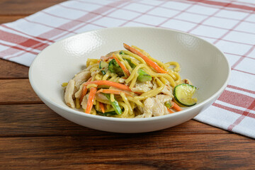 Staple food Noodle salad with carrots and zucchini on a wooden table