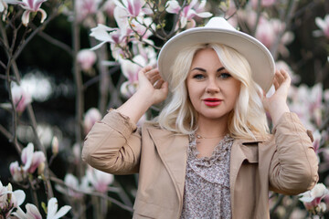 Magnolia flowers woman. A blonde woman wearing a white hat stands in front of a tree with pink flowers. She has a smile on her face and she is enjoying the beautiful scenery.