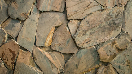 close-up perspective of a stone wall, composed of stones in a variety of shapes and sizes, predominantly in shades of gray with some brown undertones. The stones are arranged without a uniform pattern