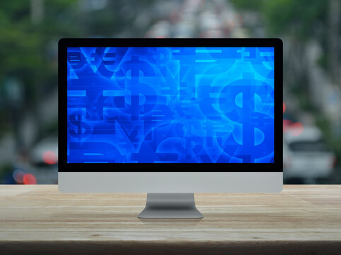 Financial currency symbol on desktop computer monitor screen on wooden table over blur of rush hour with cars and road in city