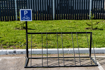 Empty bicycle parking rack in outdoor lot with green grass and fence on a sunny day. This metal...
