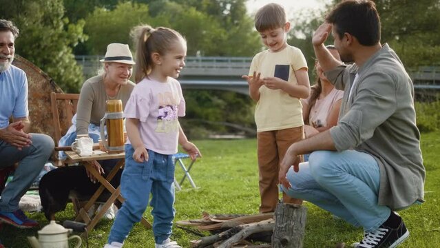 Children bring firewood to dad and help him start a fire during family camping in nature