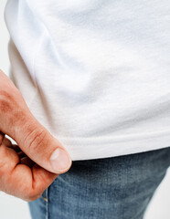 A person is grasping the hem of a white shirt with their fingers