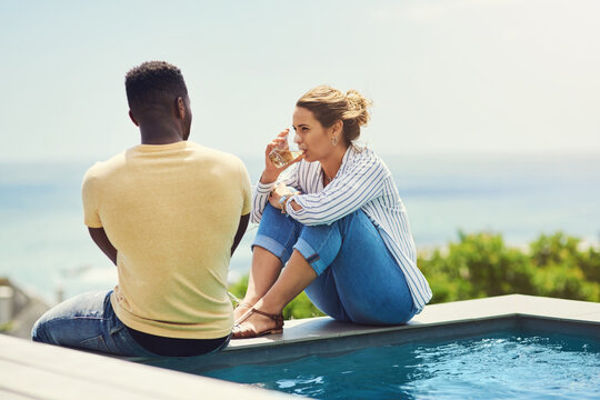 Couple, poolside and drinking alcohol to relax, bonding and together for love or talking. People, travel and speaking on holiday or vacation, juice and trees with conversation for peace and calm trip - Powered by Adobe