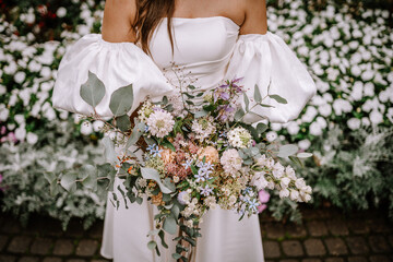 Riga, Latvia, - August 26, 2024 - Close-up of a bride holding a colorful bouquet, with a white floral background.