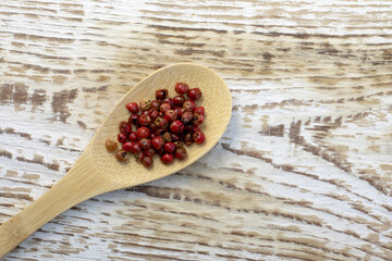 Red or pink peppercorns on wooden spoon on grey textured cutting board background