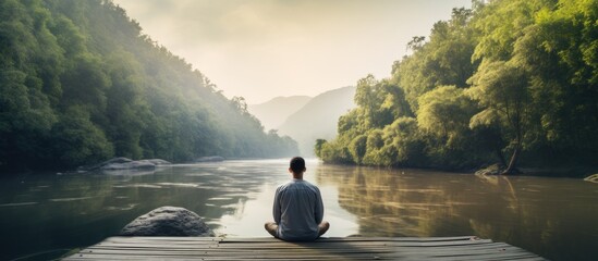 Back view of a man meditating on a wooden pier by the river with plenty of room for adding text or...