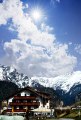 Sky with Radiant Sun over an Alpine Chalet with Snow-Capped Peaks in the Background