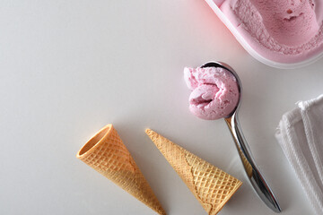 Scoop with ball of strawberry icecream with cones and tub