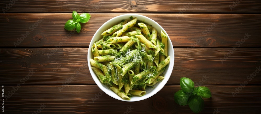Poster top view of penne pasta with pesto sauce on a wooden table providing ample copy space for additional