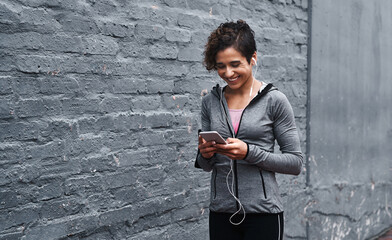 Woman, cellphone and earphones in city with wall background for relax texting, exercise or digital...