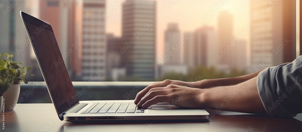 Poster A close up of hands typing on a laptop placed on a wooden desk with a stack of papers nearby against the backdrop of a window The laptop screen is blank providing ample copy space