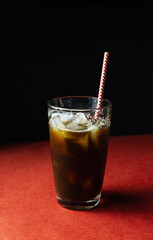 Cold coffee with ice and straw in glass on red and black background