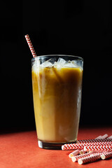 Iced coffee in glass near drinking straws on red and black background