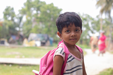 Rural School boy with backpack wearing round neck t shirt dress standing outdoor