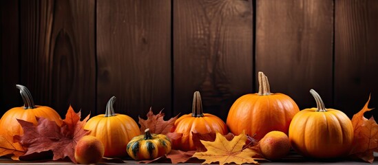 An autumn themed image featuring pumpkins and leaves placed on a wooden background leaving room for additional content
